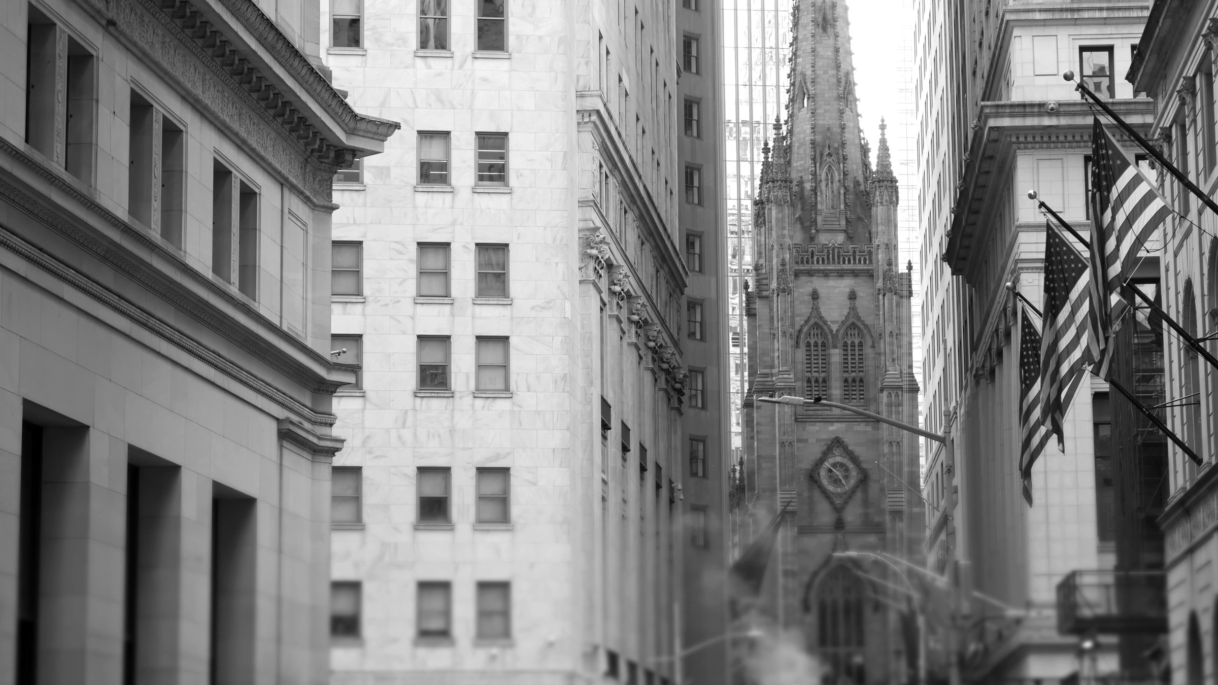 American flags flying on a building along a Lower Manhattan street, with Trinity Church beyond.